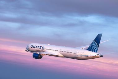 A United Airlines-branded plane flies in front of a sunset.