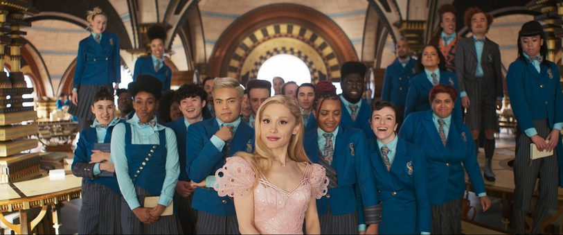 Actor Ariana Grande in costume for the film, Wicked (2024) in front of a large group of students in uniform