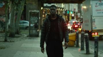 Still from A Brixton Tale. A young man walking on the side of a busy street.