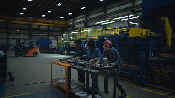 Still from Black To Techno featuring three performers in an industrial setting at a mixing desk