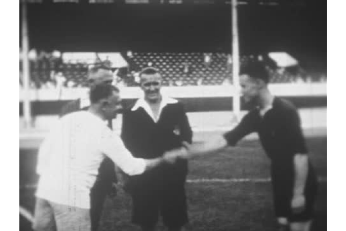 Two male footballers shake hands on the pitch at the start of a football match