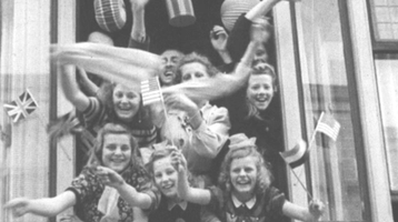 Still of people waving flags out of a window in celebration of Victory in Europe Day