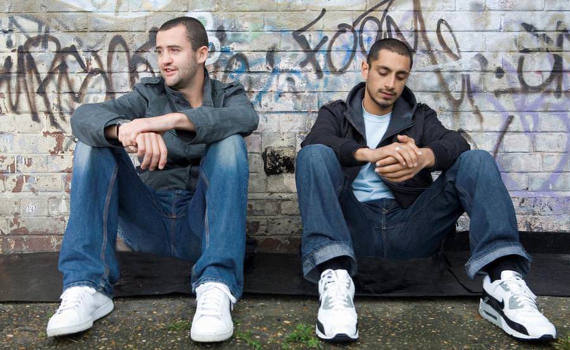 Still of Shifty. Two men sit on the floor against a wall.