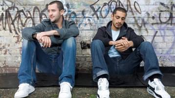 Still of Shifty. Two men sit on the floor against a wall.