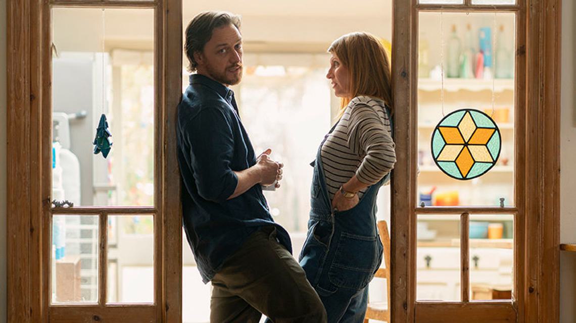 Still of Together. Two people stand in a doorframe with one looking directly at the camera