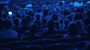 An audience in the dark in a cinema, shot from behind.