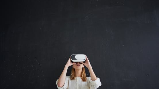 A woman on a black background in a white shirt looking into a 3D gaming headset.